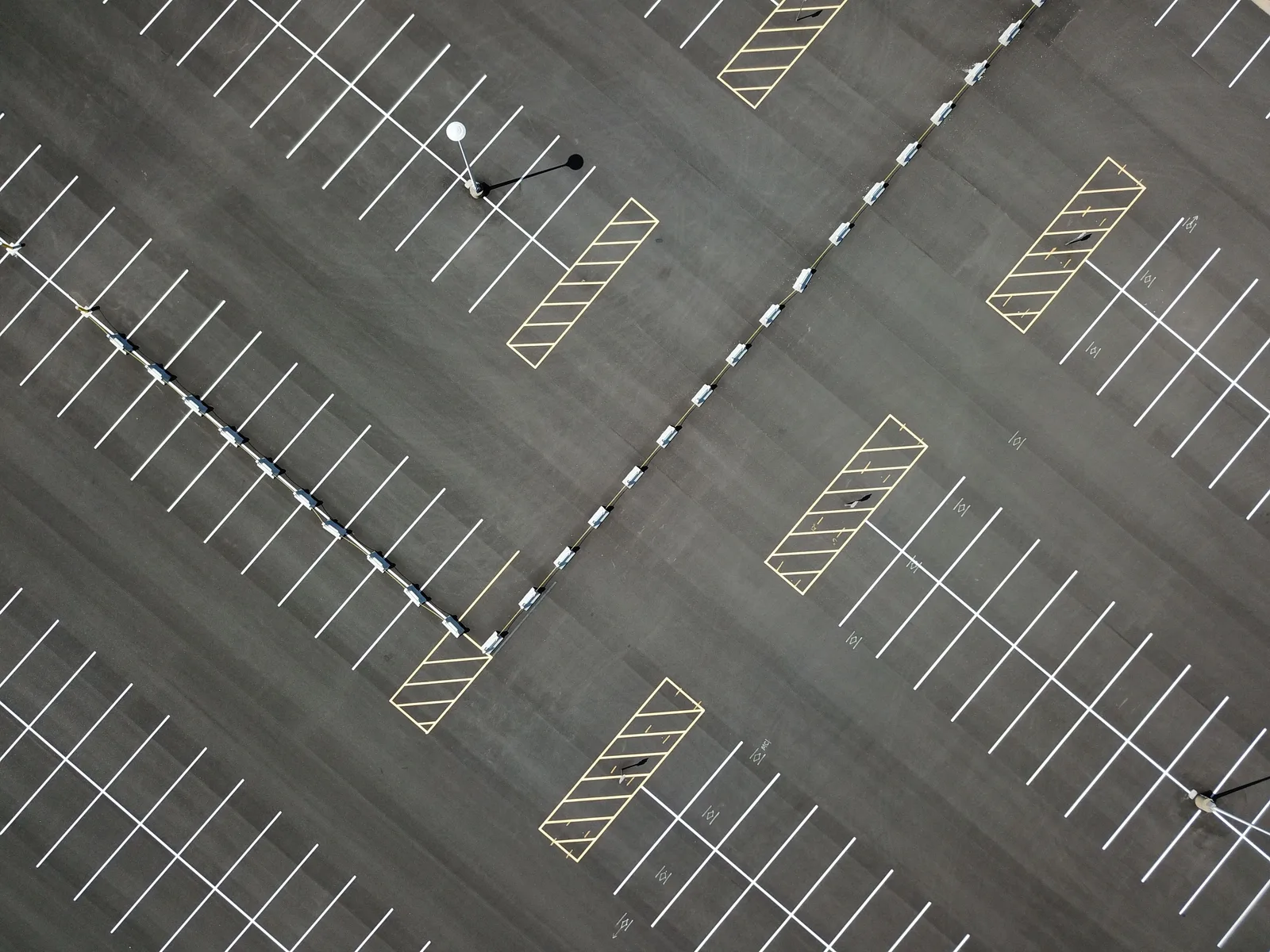 Top-down view of a large, empty parking lot featuring clear lines and patterns. Parking lot striping expansion: four growth moves, what each breaks, and how to sequence them