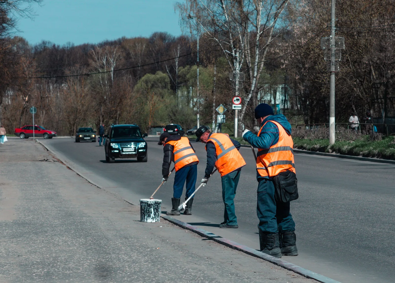 Three road workers in reflective vests paint street markings on a suburban road. Parking lot striping staff costs explained
