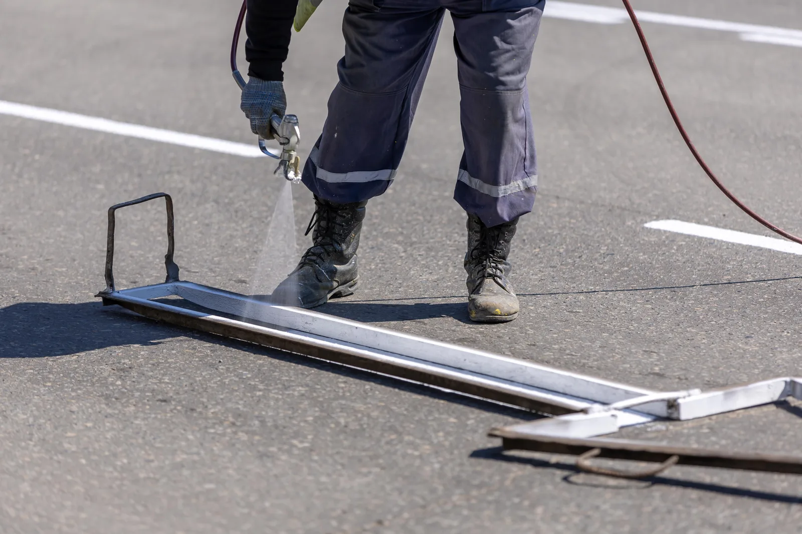 A construction worker painting white lines on a road with a spray gun during the day. Parking lot striping prices and margins for owners in 2027