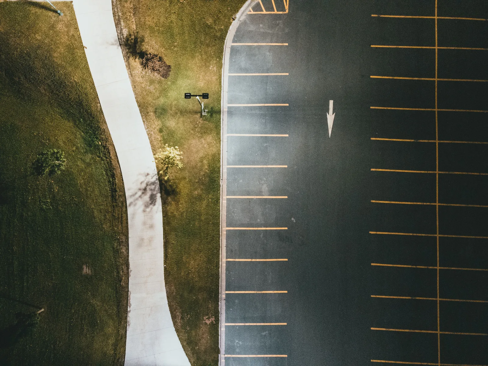 Top-down view showing an empty parking lot with marked spaces and adjacent pathway in daylight. Parking lot striping service quality rated on what actually matters