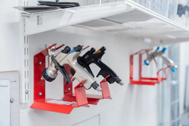 Three spray guns neatly organized on red wall mounts in a well-lit workshop setting. What to put in a parking lot striping business package for new owners